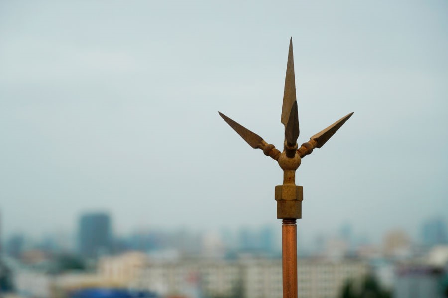 Weathered metal spike ornament against a hazy cityscape sky, muted brown and grey.